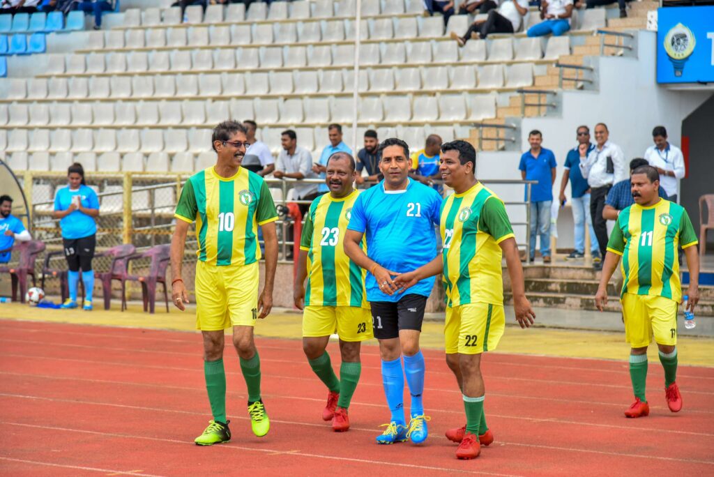 Players in green and yellow kits walking along the stadium track after the anniversary match.